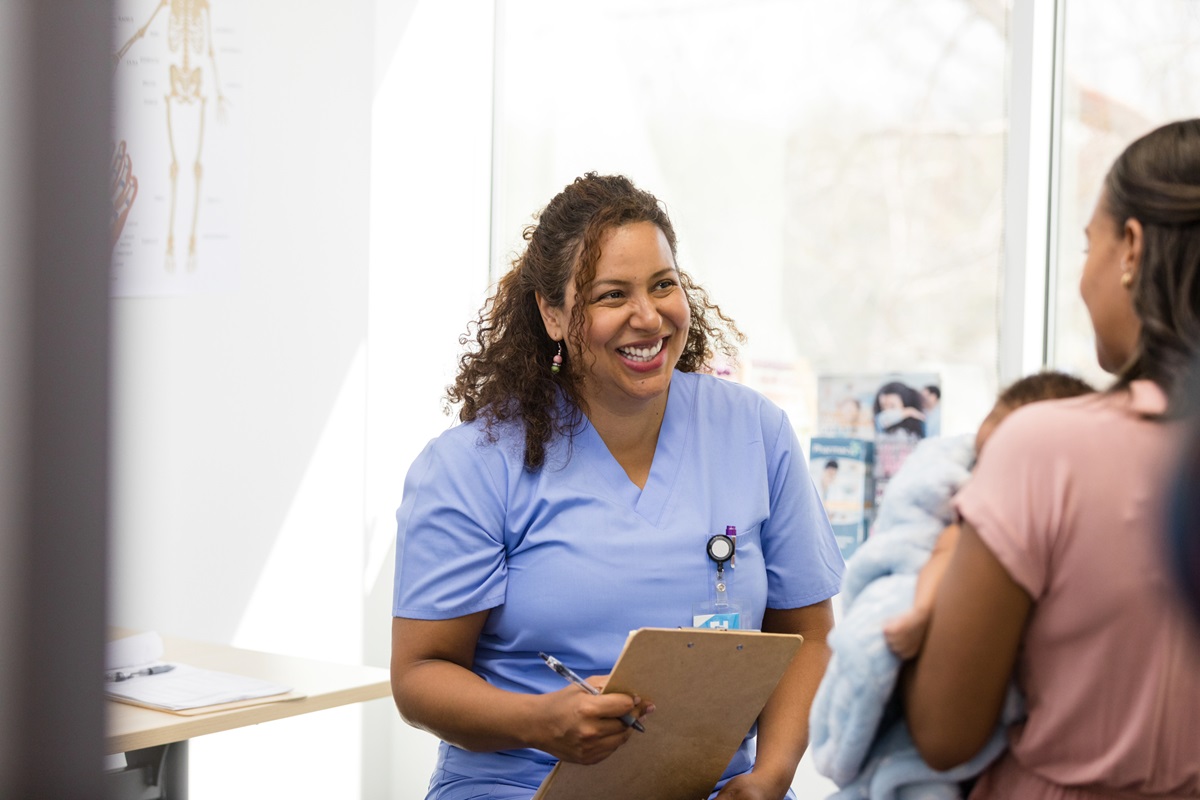 Smiling nurse and unrecognizable new mom talk about new baby.