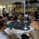 A group of people sits at a table under a patio pavilion.