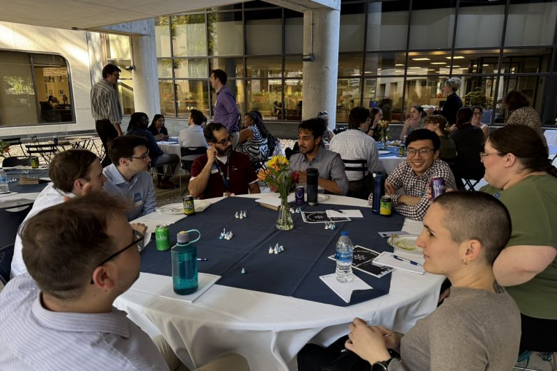 A group of people sits at a table under a patio pavilion.