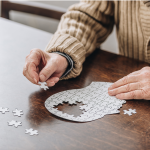 Cropped view of an elderly individual working on a puzzle shaped like a human head.