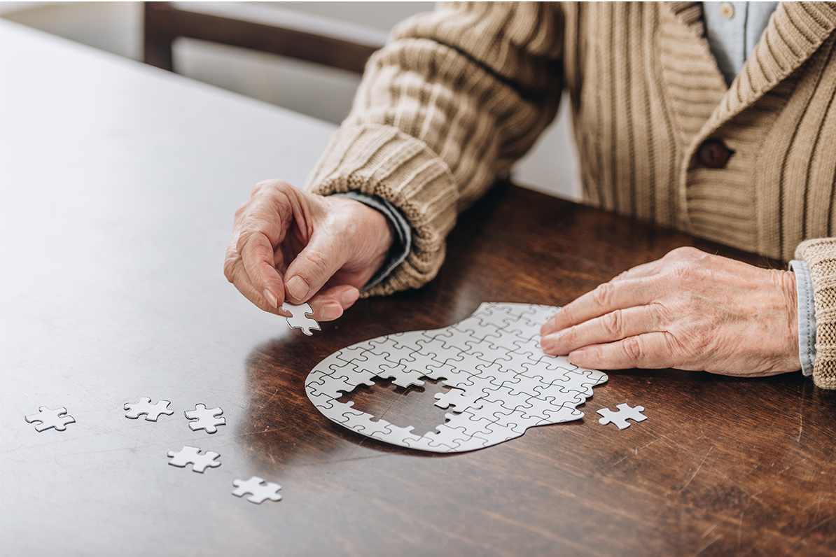 Cropped view of an elderly individual working on a puzzle shaped like a human head.