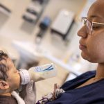 Emonie Castro, a NICU nurse, gently feeds an infant with a bottle, holding the baby close in a hospital room at Penn State Health Golisano Children’s Hospital.
