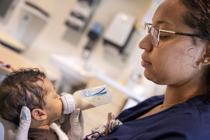 Emonie Castro, a NICU nurse, gently feeds an infant with a bottle, holding the baby close in a hospital room at Penn State Health Golisano Children’s Hospital.