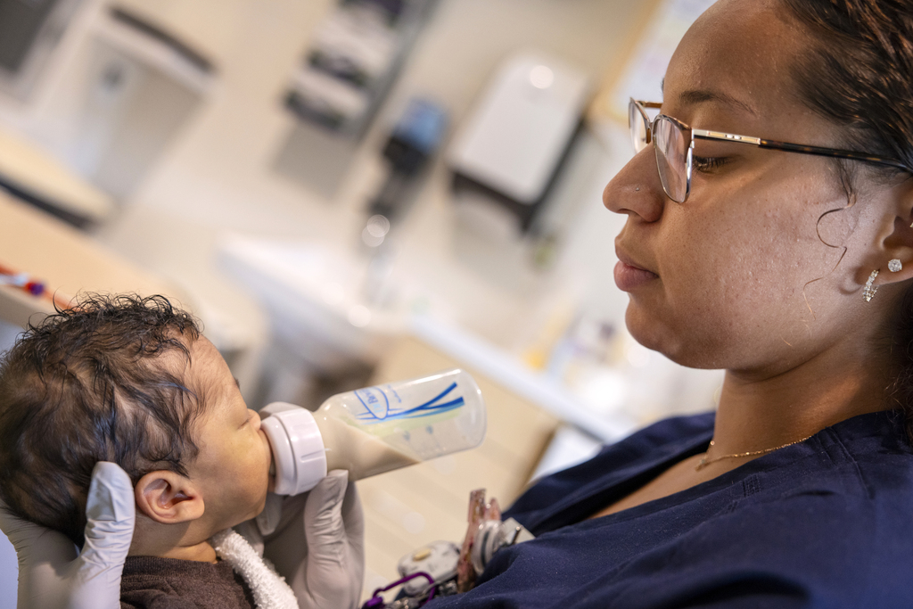 Emonie Castro, a NICU nurse, gently feeds an infant with a bottle, holding the baby close in a hospital room at Penn State Health Golisano Children’s Hospital.