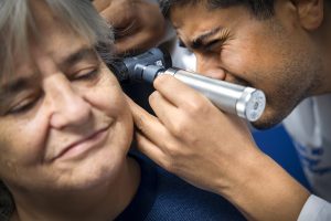 A doctor looks through an otoscope to examine a woman patient’s inner ear. 