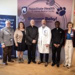 A group of eight people pose for a photo at the Breidegam Family Birthing Center at St. Joseph Medical Center. They stand in front of two banners. The one behind them reads “Penn State Health St. Joseph Medical Center” and “Welcome Baby!”