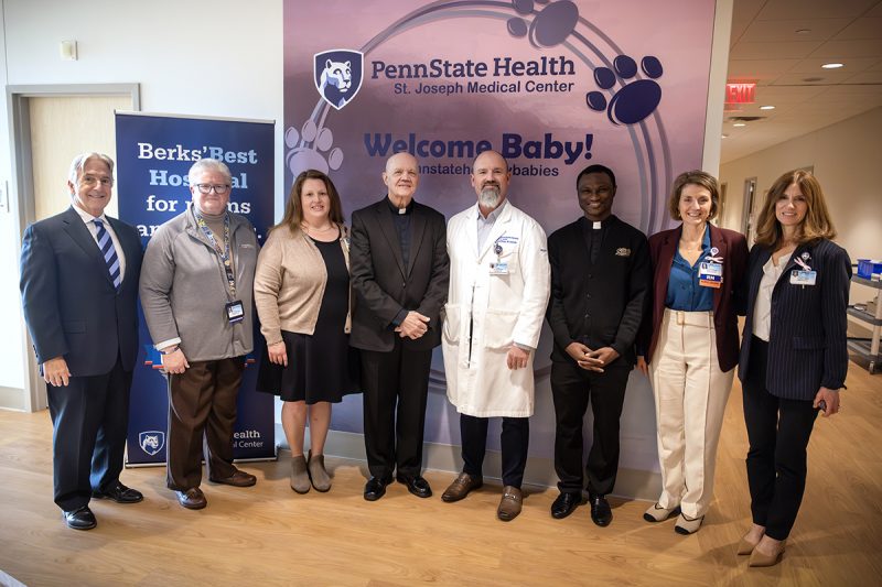 A group of eight people pose for a photo at the Breidegam Family Birthing Center at St. Joseph Medical Center. They stand in front of two banners. The one behind them reads “Penn State Health St. Joseph Medical Center” and “Welcome Baby!”