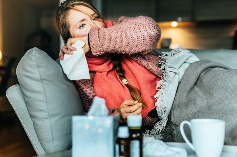 Woman coughing on a sofa and holding a tissue while sick with the flu.