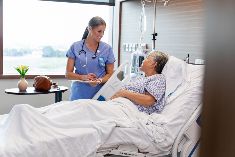 Doctor speaking with person lying in hospital bed.