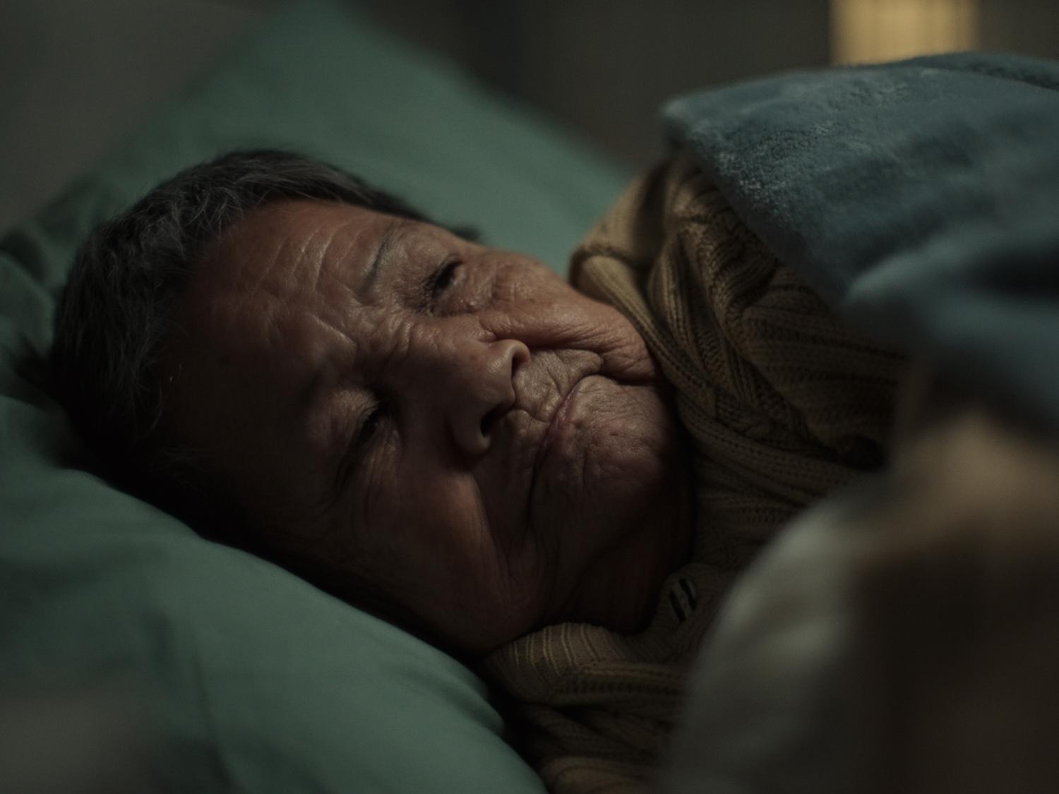 Close-up of an elderly woman lying awake in a dark room