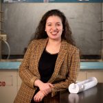 A professional portrait of Corinne Augusto, with a research lab in the background.