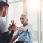 Older man doing hand therapy exercises with a physical therapist