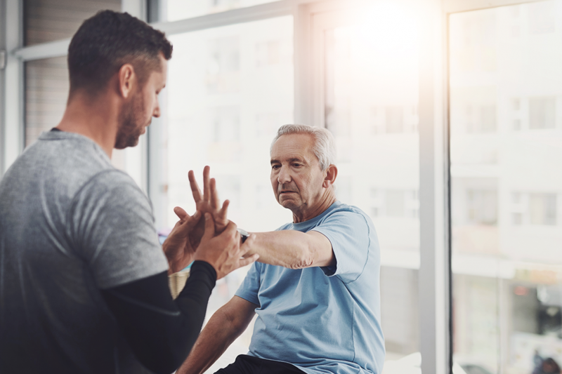 Older man doing hand therapy exercises with a physical therapist