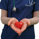 Torso of a health care working wearing scrubs, hands held out holding a symbolic heart.