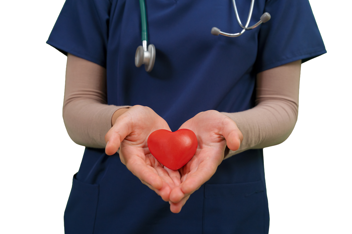 Torso of a health care working wearing scrubs, hands held out holding a symbolic heart.