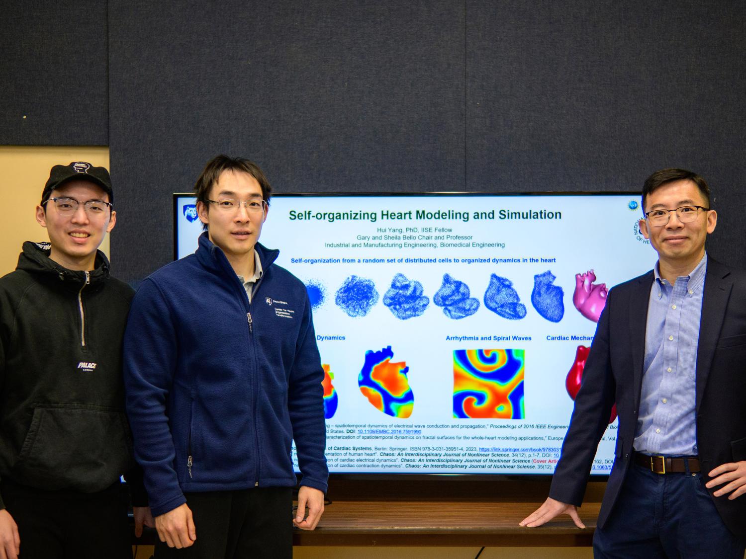 Three men pose for a photo in front of a television that reads 