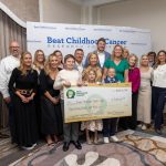 A group of adults and children pose with an oversized check in the amount of $3 million. A backdrop contains the Beat Childhood Cancer Research Consortium logo.