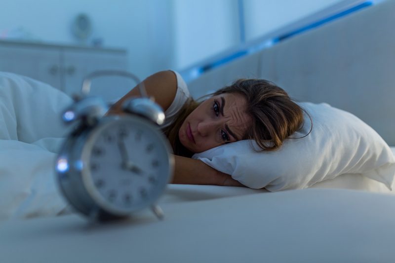 Woman with insomnia lying in bed looking at alarm clock.