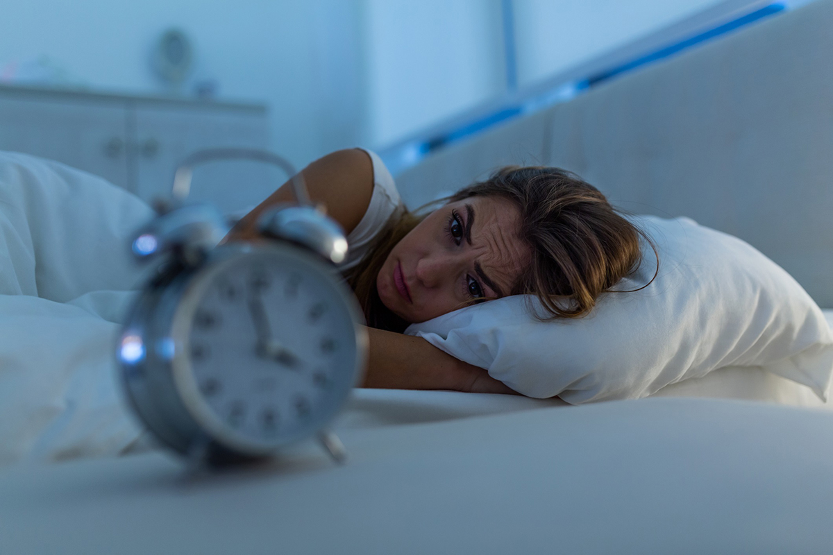 Woman with insomnia lying in bed looking at alarm clock.