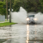 A truck driving on a flooded road, kicking up a lot of water around it.