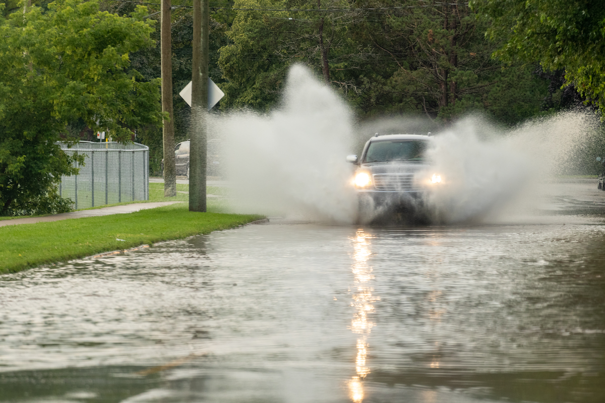 A truck driving on a flooded road, kicking up a lot of water around it.