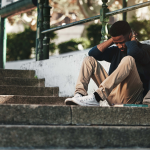 Young man with head bowed and sitting against a staircase.