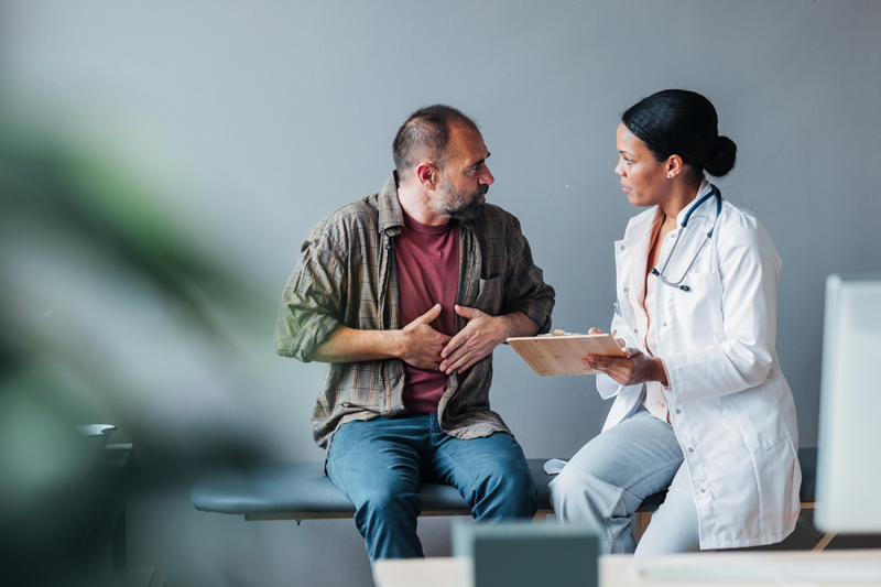 A person gesturing to their stomach and speaking with a doctor