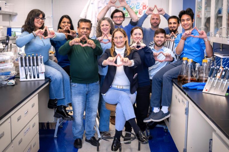 Ten people in a lab pose for a photo shaping their fingers into a triangle