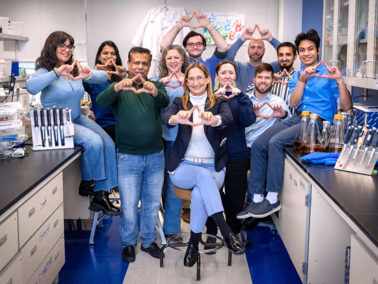 Ten people in a lab pose for a photo shaping their fingers into a triangle