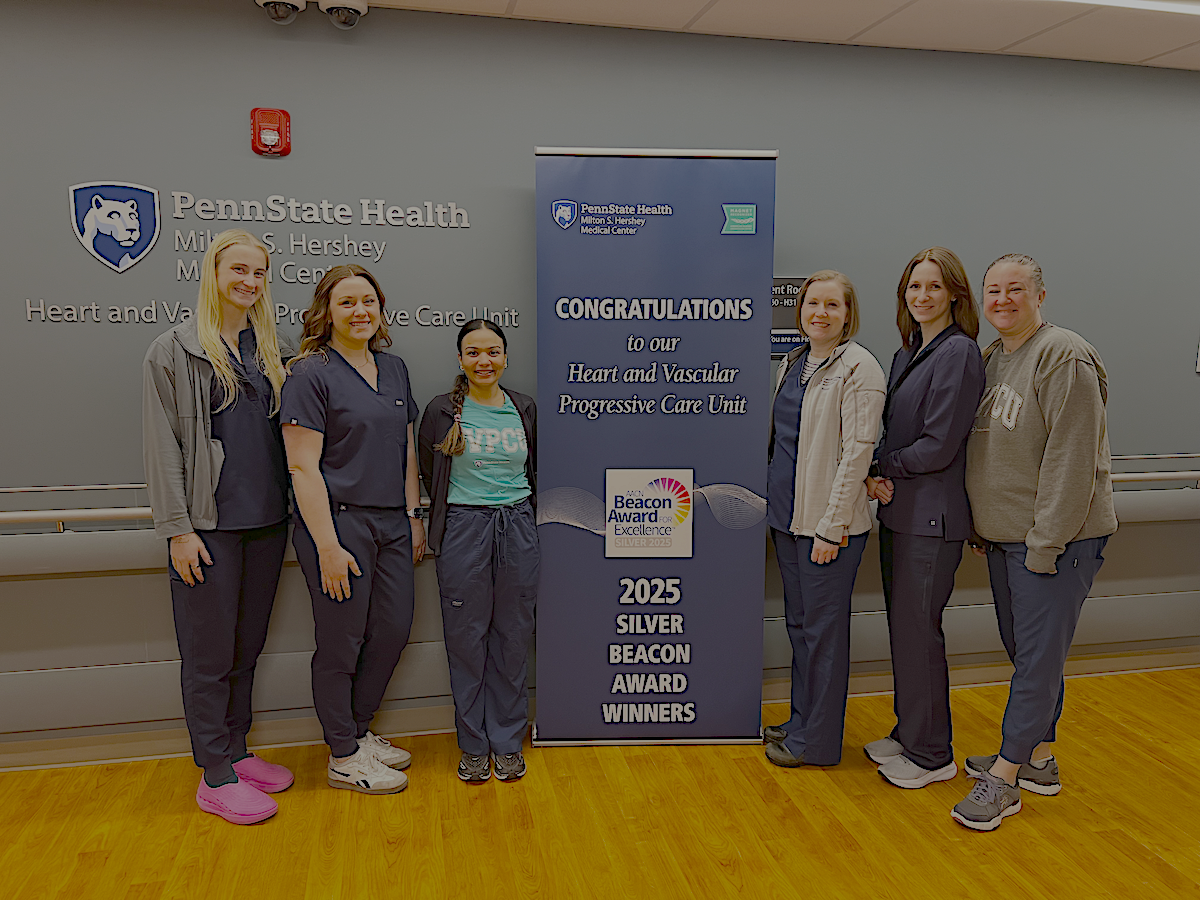 Six people pose around a sign that says, 