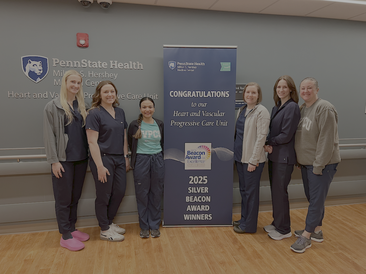 Six people pose around a sign that says, 