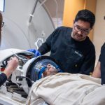 Medical team preparing a patient for a focused ultrasound procedure, with clinicians adjusting equipment around the patient’s head inside a specialized imaging device.