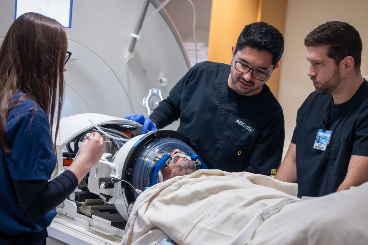 Medical team preparing a patient for a focused ultrasound procedure, with clinicians adjusting equipment around the patient’s head inside a specialized imaging device.
