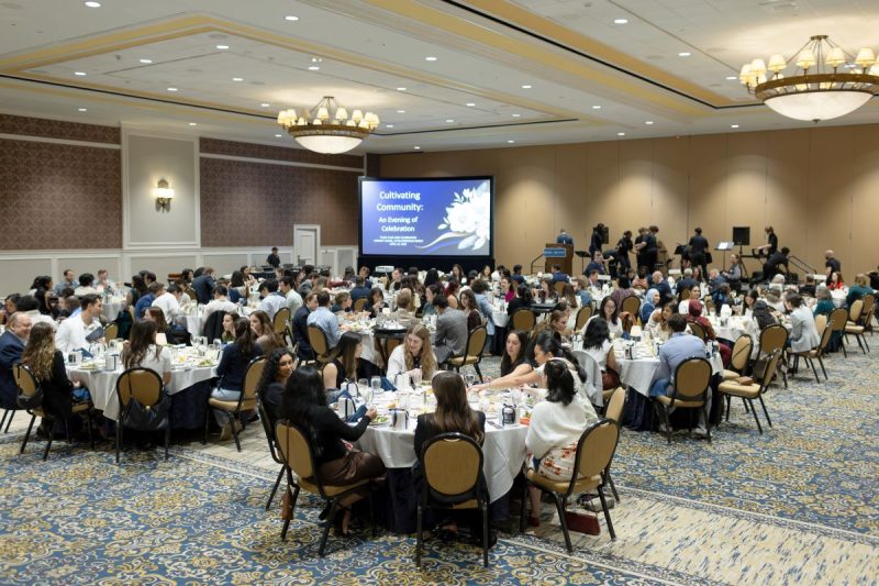 Students, faculty, staff and community partners sit at round banquet tables during the OHACE year-end celebration at Hershey Lodge, facing a stage with a screen displaying the words “Cultivating Community: An Evening of Celebration.”