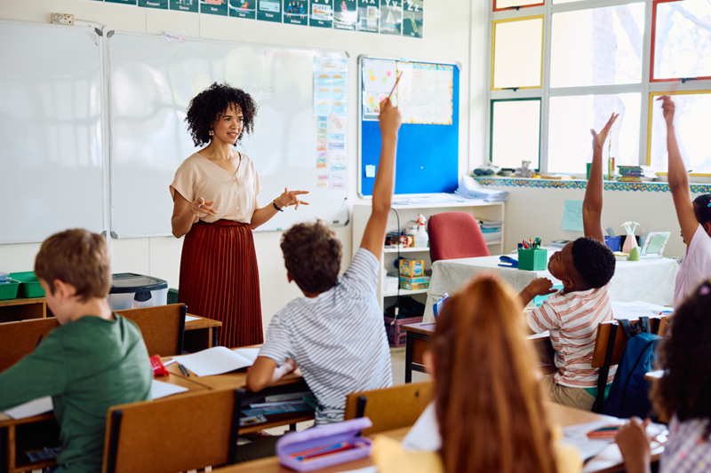 Teacher stands at the front of a classroom full of children.