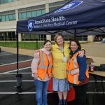 Two canopies branded Penn State Health Milton S. Hershey Medical Center are set up along the road in front of the medical center. Hospital staff stand under and around the canopies, facing the road.