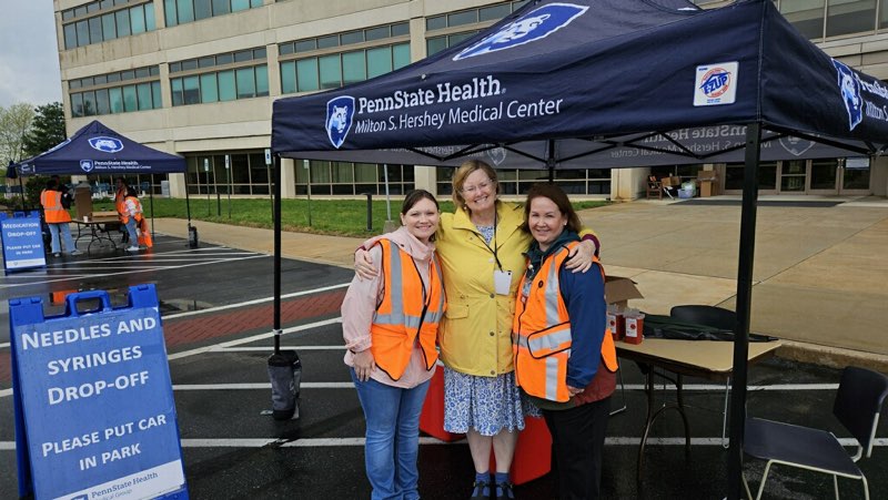 Two canopies branded Penn State Health Milton S. Hershey Medical Center are set up along the road in front of the medical center. Hospital staff stand under and around the canopies, facing the road.