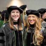Two students pose for a photo in their graduation regalia