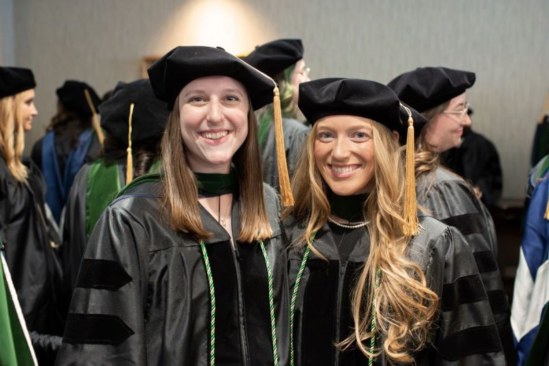 Two students pose for a photo in their graduation regalia