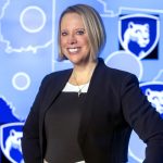 Dr. Jennifer Kraschnewski poses for a photograph, wearing professional attire. The background is a map with several Penn State Nittany Lion shield logos.