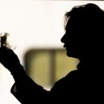 This photo shows a silhouette of Nick Zawatsky in a research lab holding a beaker.
