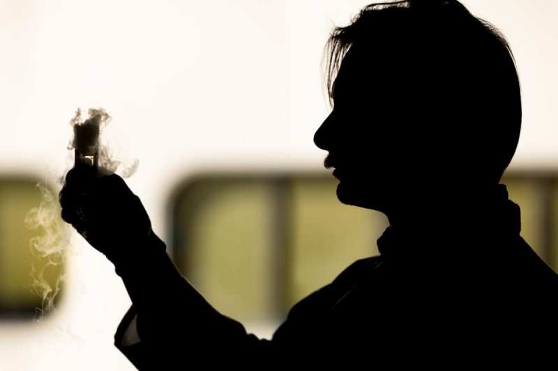 This photo shows a silhouette of Nick Zawatsky in a research lab holding a beaker.