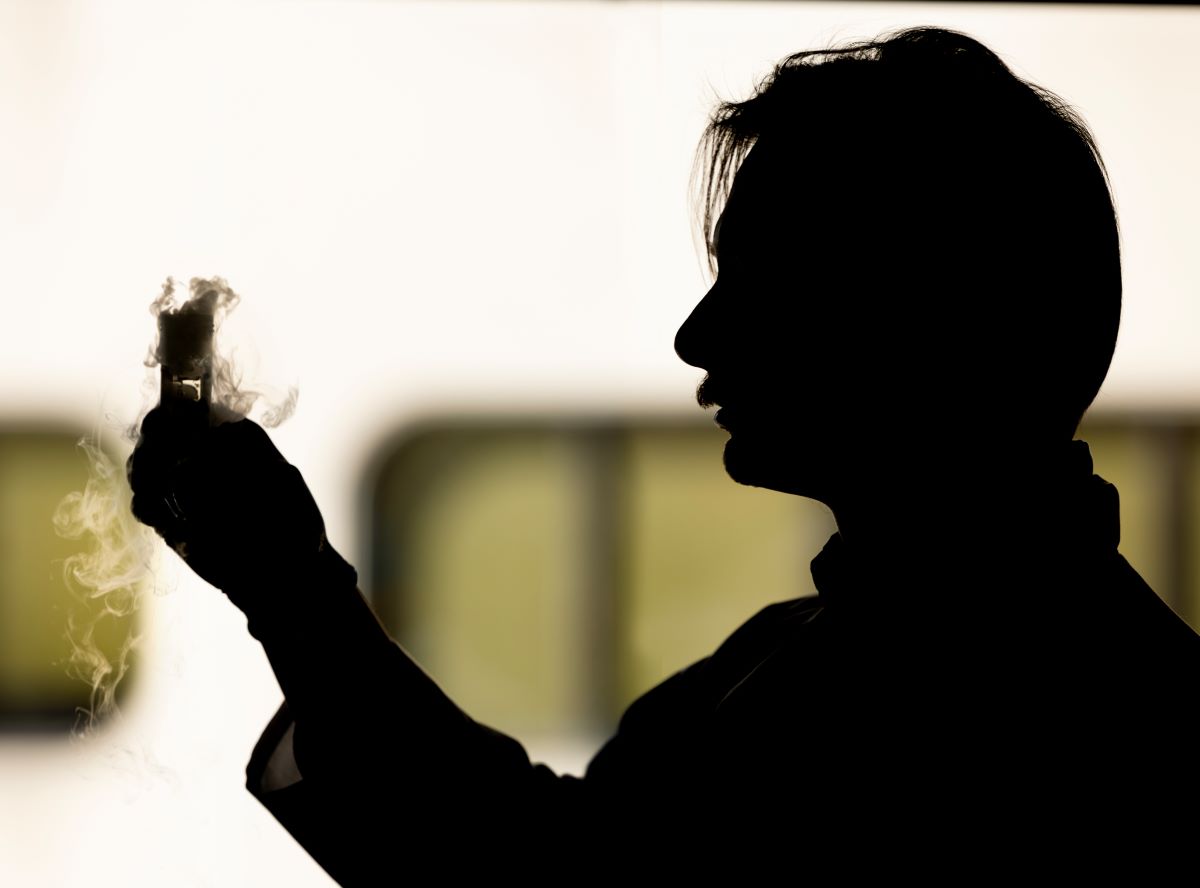 This photo shows a silhouette of Nick Zawatsky in a research lab holding a beaker.