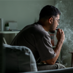An individual sitting on a couch uses an e-cigarette.