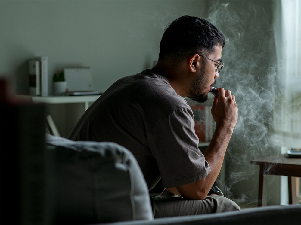 An individual sitting on a couch uses an e-cigarette.