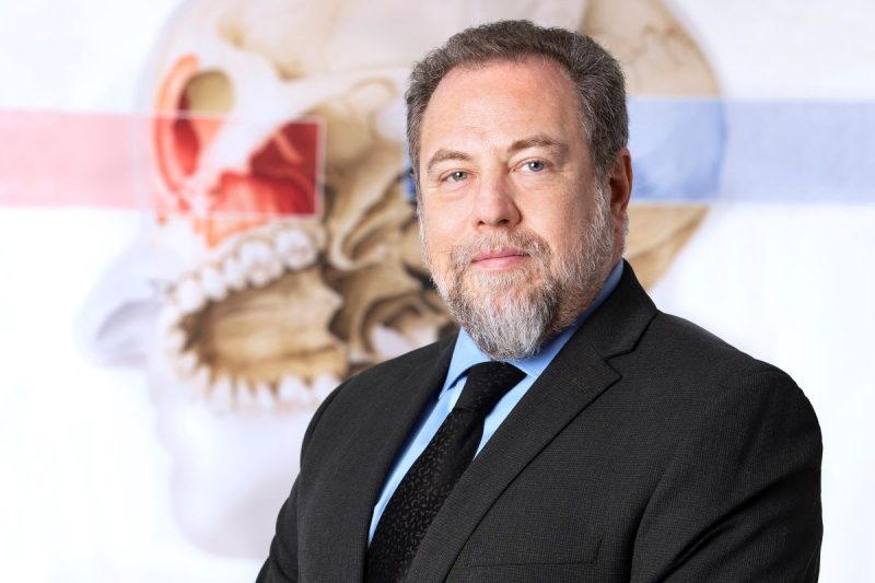 A head-and-shoulders professional headshot of Dr. David Goldenberg, with a diagram of the ear, nose and throat in the background.