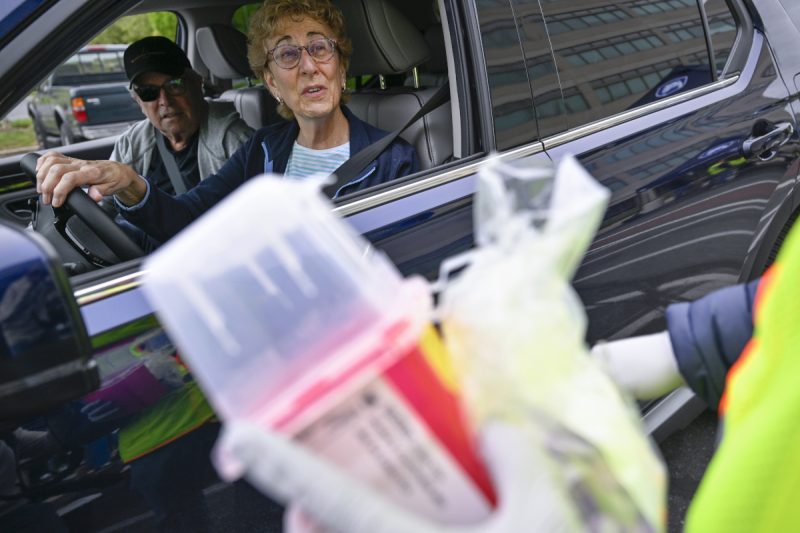A man and woman sitting in a car talk to a person at Penn State Health’s Prescription Drug Take-Back Day. The person holds a sharps container and is wearing a safety jacket and coat.