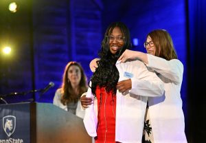 Brianna Dawes receives her white physician coat on stage during a ceremony.
