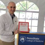 Dr. Michael McShane holds a framed award while standing at a podium.
