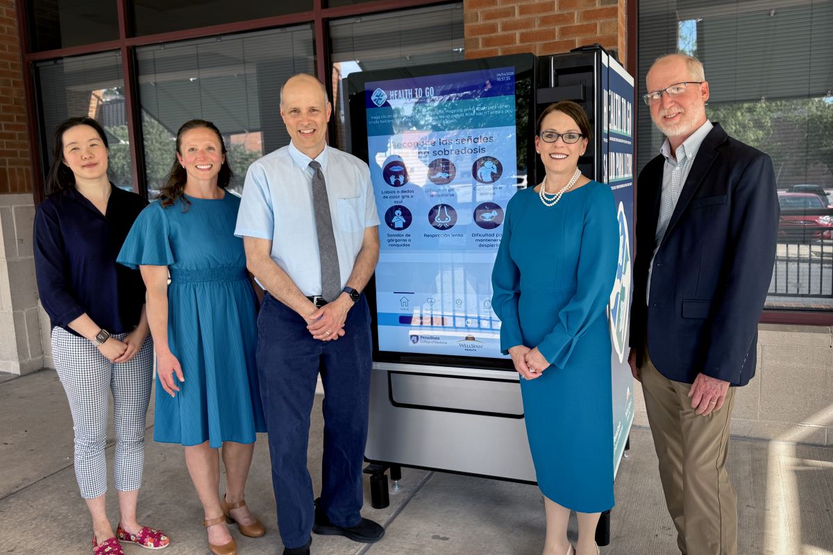 A group of people stands in front of a vending machine with a digital display screen of health items.